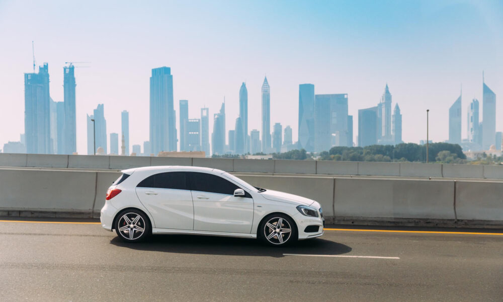 a side-angle shot of a Mercedes-Benz A-Class parked on the roadside with Dubai skyscrapers in the background