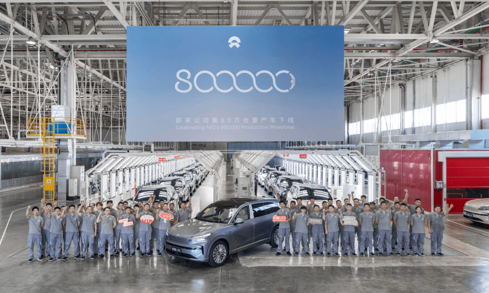 a front-angle wide shot of a group of NIO factory workers celebrating the brand's production milestone