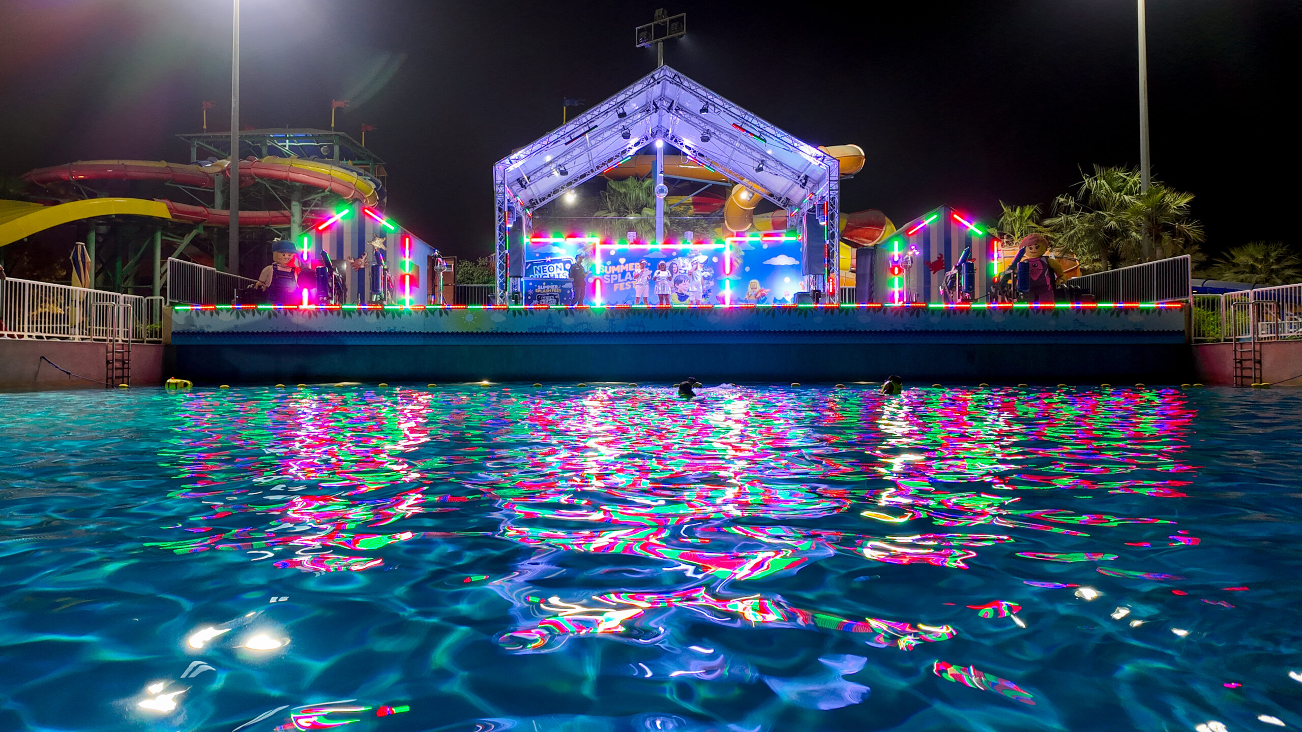 LEGOLAND Dubai Water Park’s Neon Nights event with a glowing stage, vibrant neon lights reflecting on the wave pool, and themed LEGO decorations.