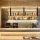 Modern restaurant bar featuring large-format ceramic slabs, wood slat ceiling, illuminated shelving with bottles, and marble-effect surfaces.
