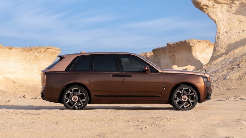 A side-angle shot of the Rolls-Royce Black Badge Cullinan Series II Desert Sunset parked in the desert.