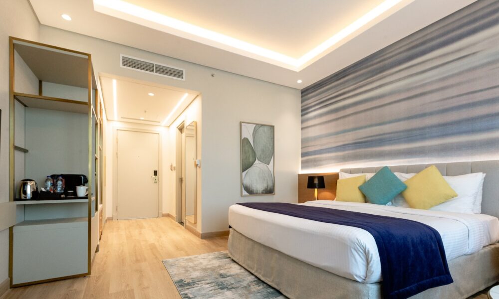 Modern hotel room featuring contemporary interior design with striped accent wall, teal and yellow pillows, and sleek furnishings showcasing Creative Wrap renovation work.