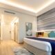Modern hotel room featuring contemporary interior design with striped accent wall, teal and yellow pillows, and sleek furnishings showcasing Creative Wrap renovation work.