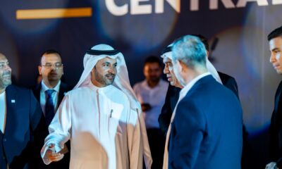 Group of business leaders in formal attire conversing at an event, with one man in traditional Emirati dress at the center