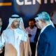 Group of business leaders in formal attire conversing at an event, with one man in traditional Emirati dress at the center