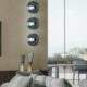Modern living room interior with wall art, decorative lighting fixtures, glass vases, and large windows overlooking greenery.