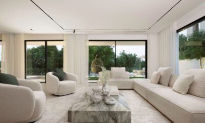 Modern minimalist living room with beige sectional sofa, marble coffee table, and floor-to-ceiling windows overlooking green landscape