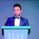 Ravi Bhirani, Managing Director of ANAX Developments, speaking at ELLE Residences Dubai Islands launch event in formal blue tuxedo at podium.