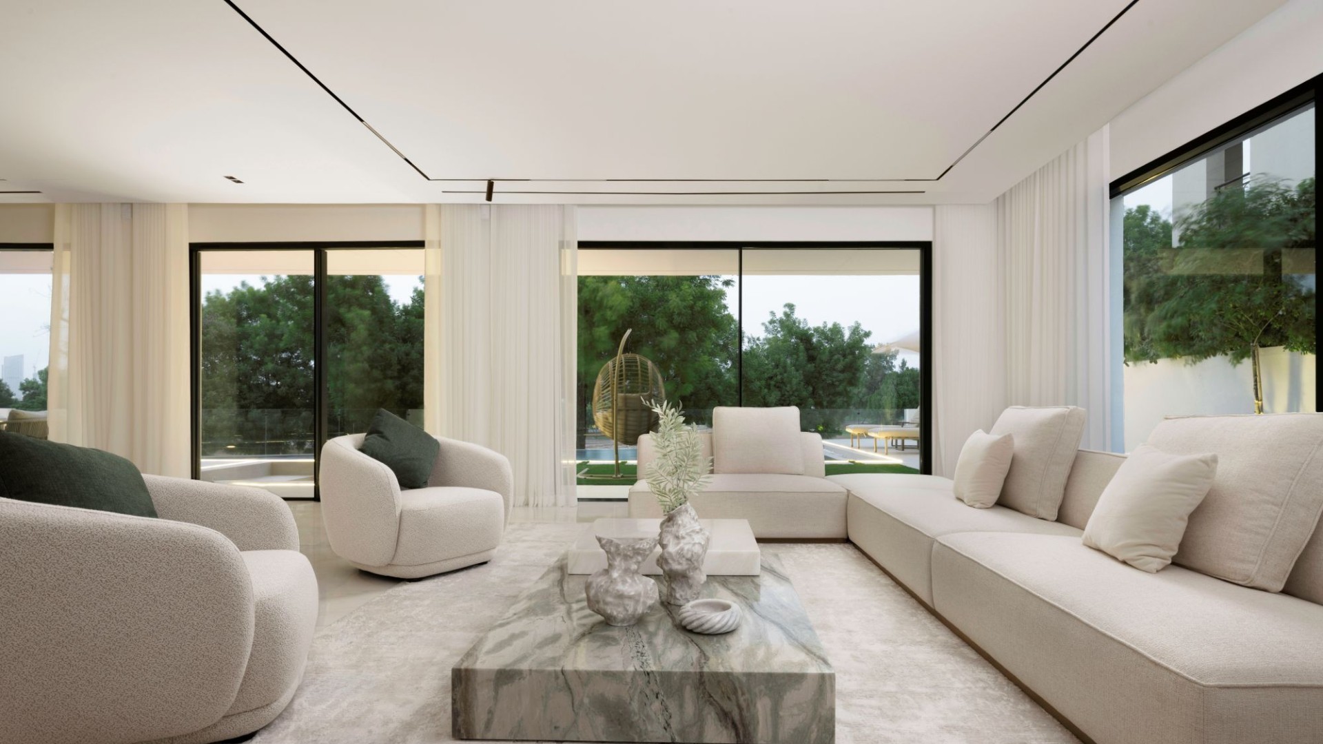Modern minimalist living room with beige sectional sofa, marble coffee table, and floor-to-ceiling windows overlooking green landscape