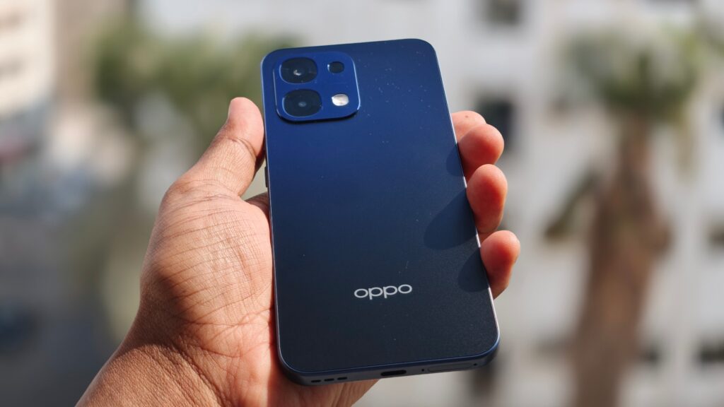 A rear-angle shot of the Oppo A6 Pro 5G held in hand with a carnival in the background