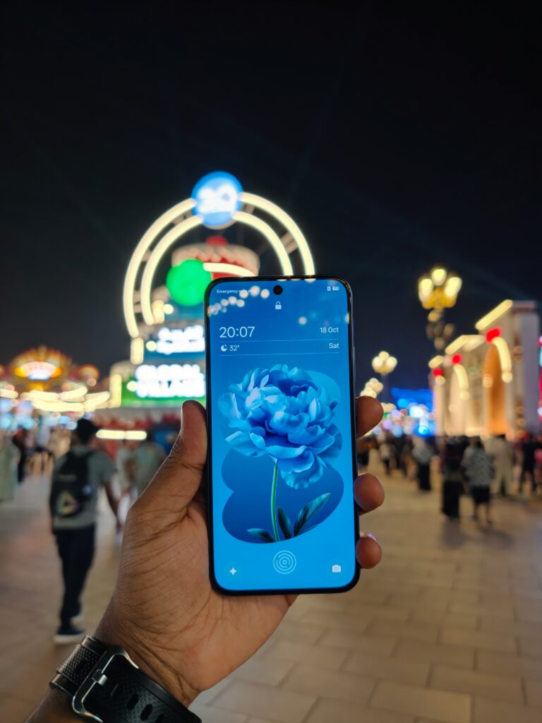 A front-angle shot of an Oppo A6 Pro 5G held in hand with a carnival in the blurred background