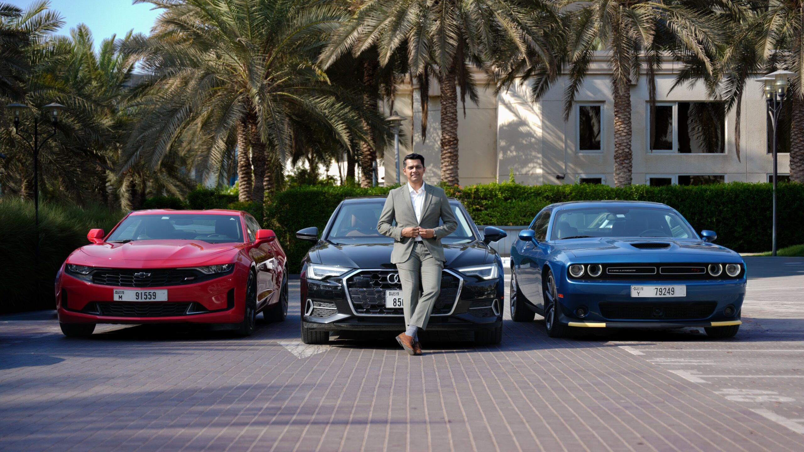 A front-angle shot of Harshvardhan Singh, Business Head, CARIVA standing in front of an Audi A6, Chevy Camaro and Dodge Charger