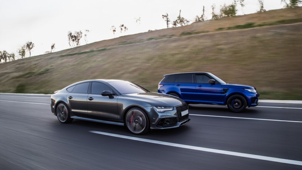 A front-three quarter action shot of a Audi RS5 and Range Rover Sport driven on the road