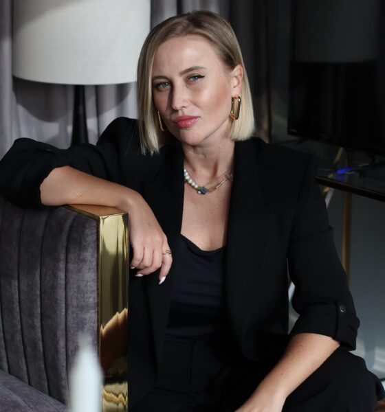 Professional portrait of Olga Pankina, Whitewill Dubai COO, wearing black blazer and seated beside gray velvet chair with gold accents in contemporary office interior