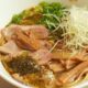 Bowl of ramen noodle soup with sliced pork, green onions, bamboo shoots, and shredded white radish in savory broth