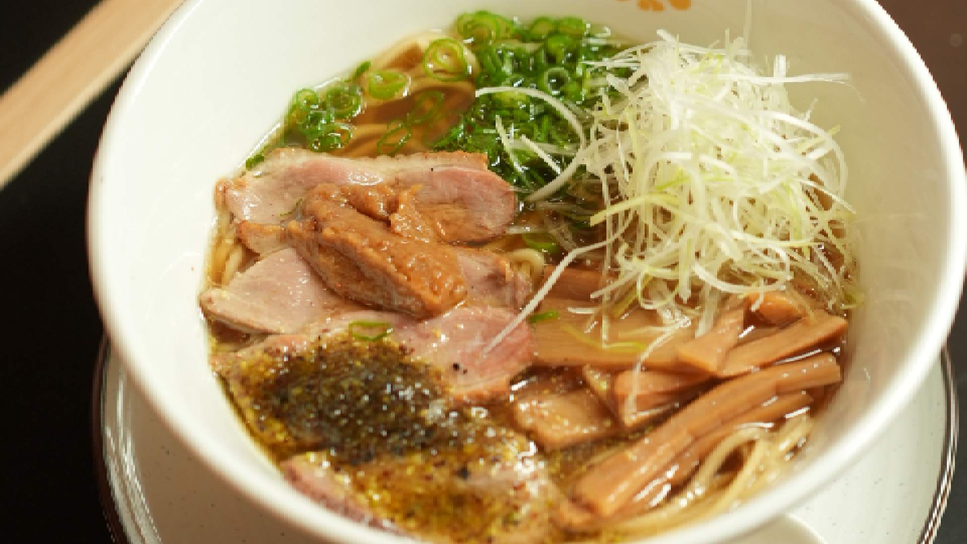 Bowl of ramen noodle soup with sliced pork, green onions, bamboo shoots, and shredded white radish in savory broth