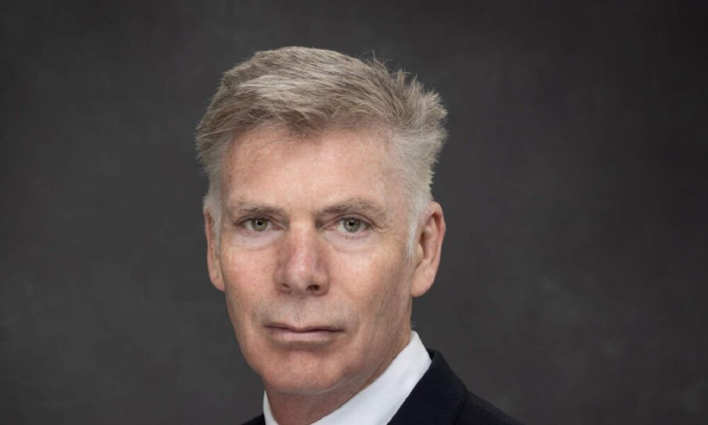Professional headshot of a businessman in dark suit and white shirt against gray background