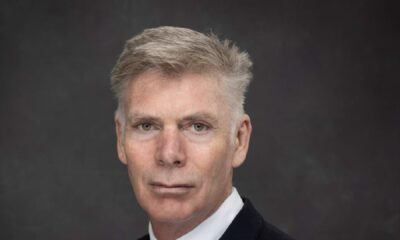 Professional headshot of a businessman in dark suit and white shirt against gray background