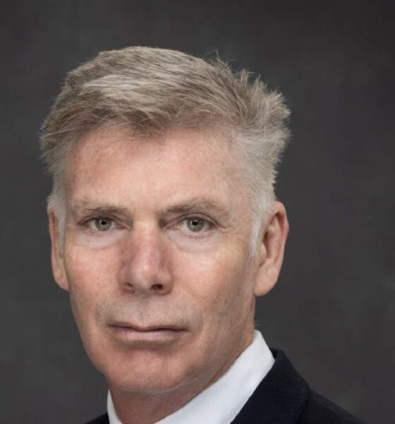 Professional headshot of a businessman in dark suit and white shirt against gray background