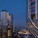 Architectural rendering of Object 1 premium high-rise residential development featuring distinctive curved metallic facade and sky terraces with Burj Khalifa visible in background during blue hour in Dubai