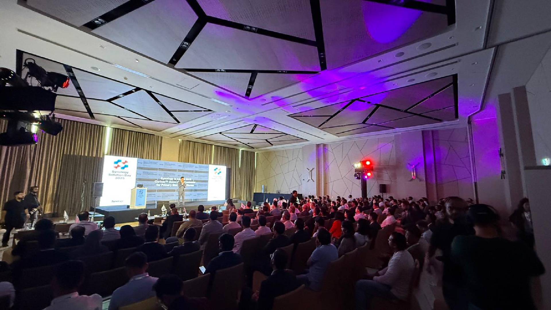Large audience at Synology UAE Solution Day event with speaker presenting enterprise data protection solutions on stage with purple ambient lighting.