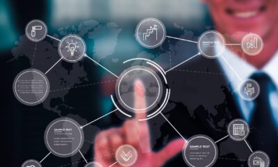 Business professional pointing at digital network interface with interconnected icons representing enterprise solutions, innovation, and global connectivity over world map background.