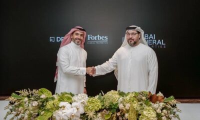 Two executives in traditional Emirati dress shaking hands at Driven Properties and Dubai General Properties Corinthia Dubai agreement ceremony with floral arrangements.