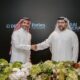 Two executives in traditional Emirati dress shaking hands at Driven Properties and Dubai General Properties Corinthia Dubai agreement ceremony with floral arrangements.