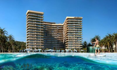 Luxurious beachfront Mondrian hotel with modern architecture, surrounded by palm trees and clear blue water where a man is paddleboarding