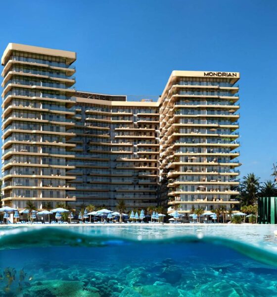 Luxurious beachfront Mondrian hotel with modern architecture, surrounded by palm trees and clear blue water where a man is paddleboarding