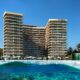Luxurious beachfront Mondrian hotel with modern architecture, surrounded by palm trees and clear blue water where a man is paddleboarding