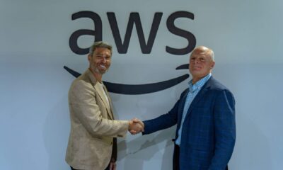 Two business executives in suits shaking hands during Tealium and AWS partnership signing ceremony at GITEX 2025 Dubai, standing before large AWS branded wall