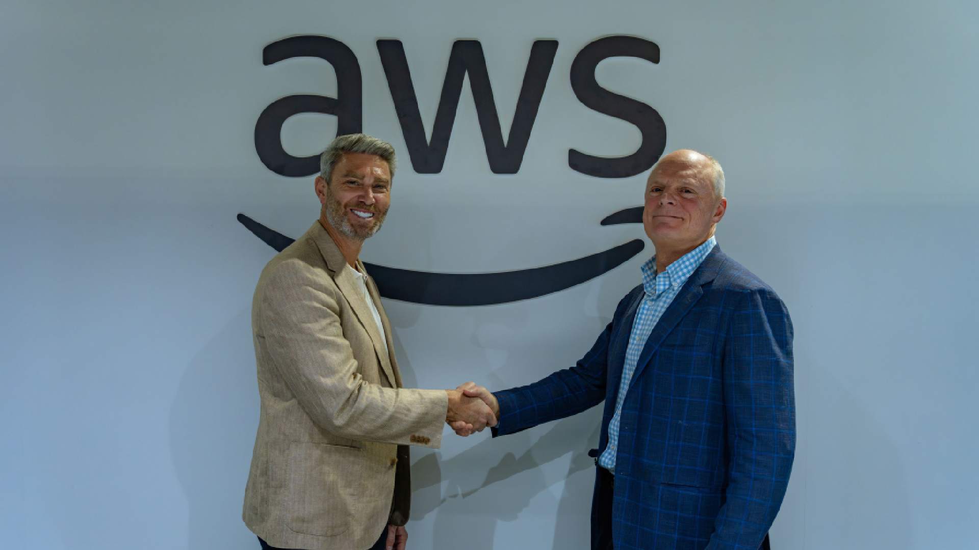 Two business executives in suits shaking hands during Tealium and AWS partnership signing ceremony at GITEX 2025 Dubai, standing before large AWS branded wall