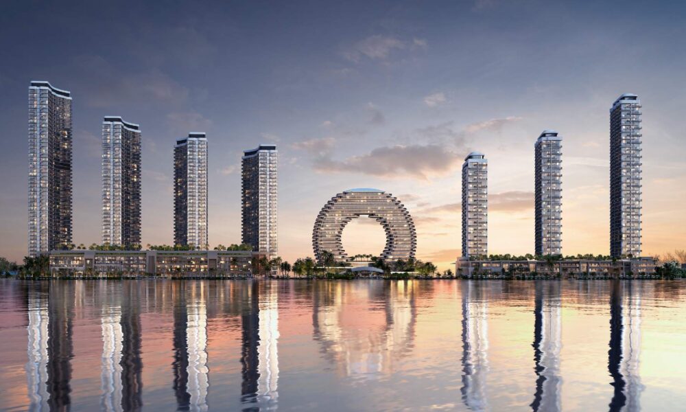Waterfront skyline with modern high-rise towers and circular architectural centerpiece reflected in calm water at sunset