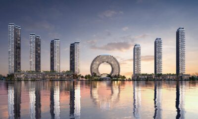 Waterfront skyline with modern high-rise towers and circular architectural centerpiece reflected in calm water at sunset