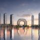Waterfront skyline with modern high-rise towers and circular architectural centerpiece reflected in calm water at sunset