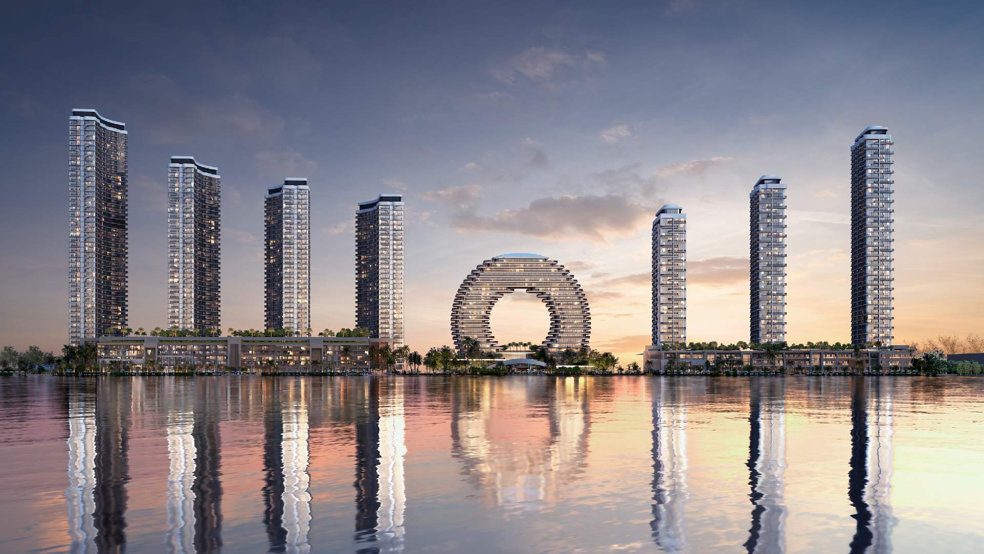 Waterfront skyline with modern high-rise towers and circular architectural centerpiece reflected in calm water at sunset