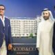 Three business professionals posing with an architectural model of Jacob & Co Residences, a modern multi-story residential building with palm trees and rooftop greenery