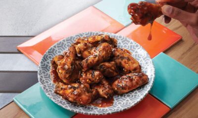 Hand holding glazed chicken wing dripping with sauce over plate of barbecue wings on geometric patterned plate