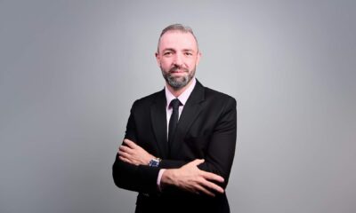 Professional businessman in black suit with arms crossed standing against gray background