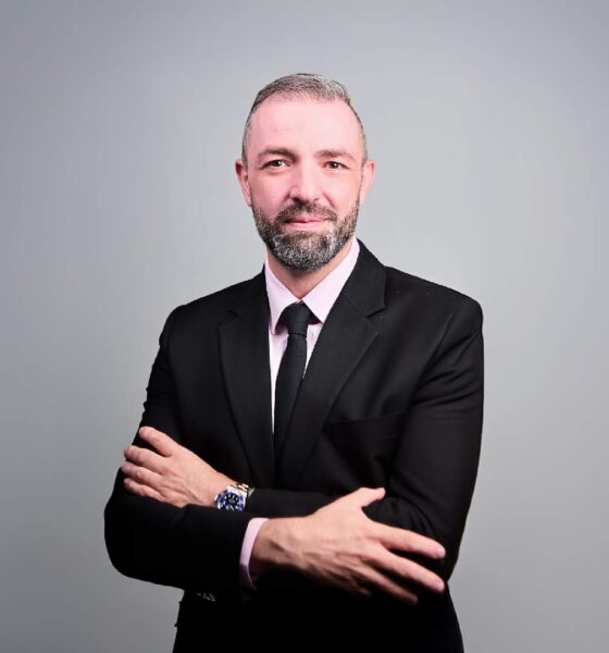 Professional businessman in black suit with arms crossed standing against gray background
