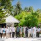 Diverse group of resort staff in white and casual attire standing together at tropical beachfront property with palm trees and thatched roof villas