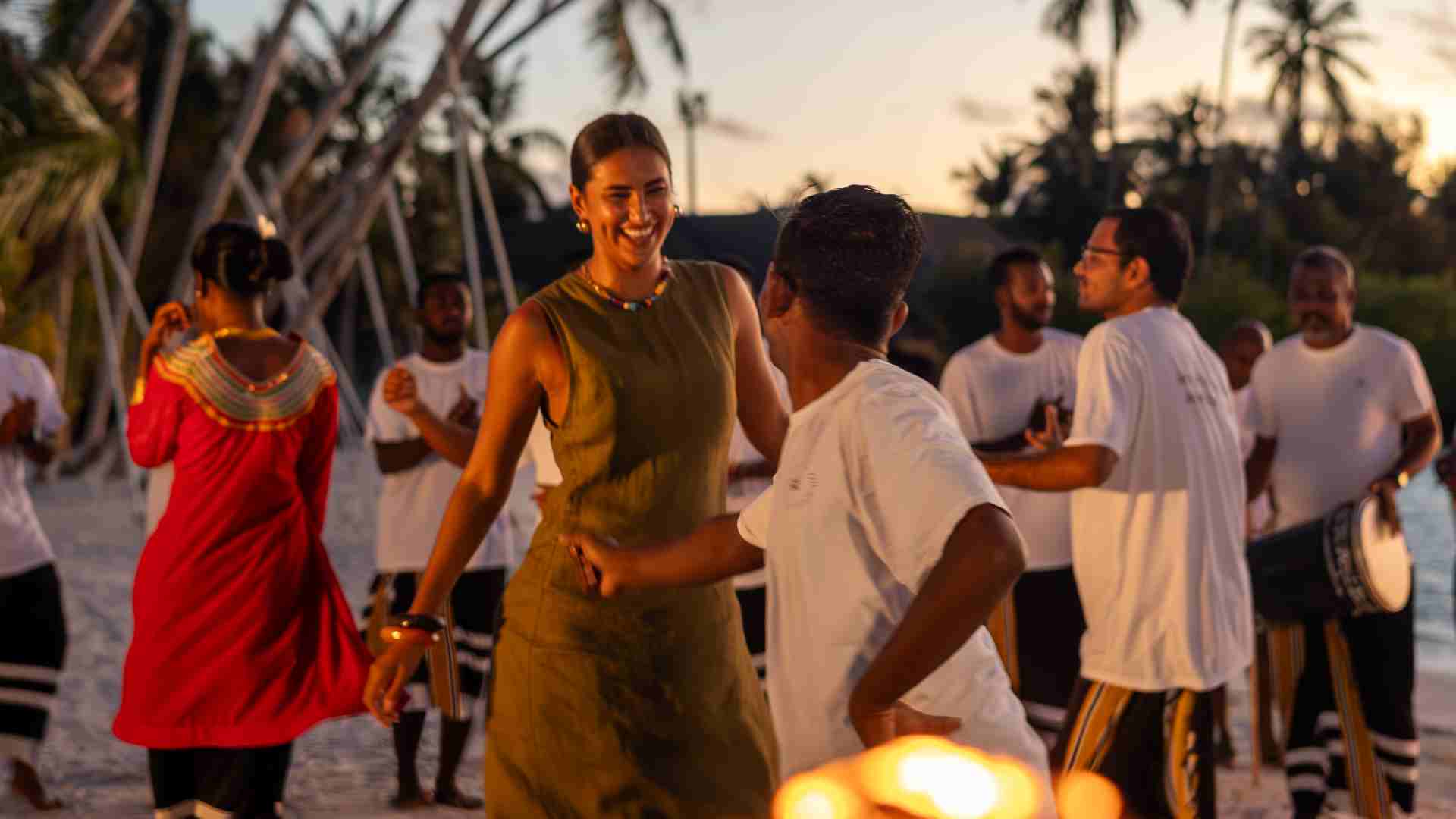 Guests dancing at sunset beach celebration with traditional Maldivian performers at Sun Siyam resort