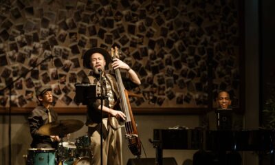 Three-piece jazz trio performing live at Cucina The Palm during Jazz and Juice Nights, featuring upright bass, piano, and drums against decorative wall backdrop.