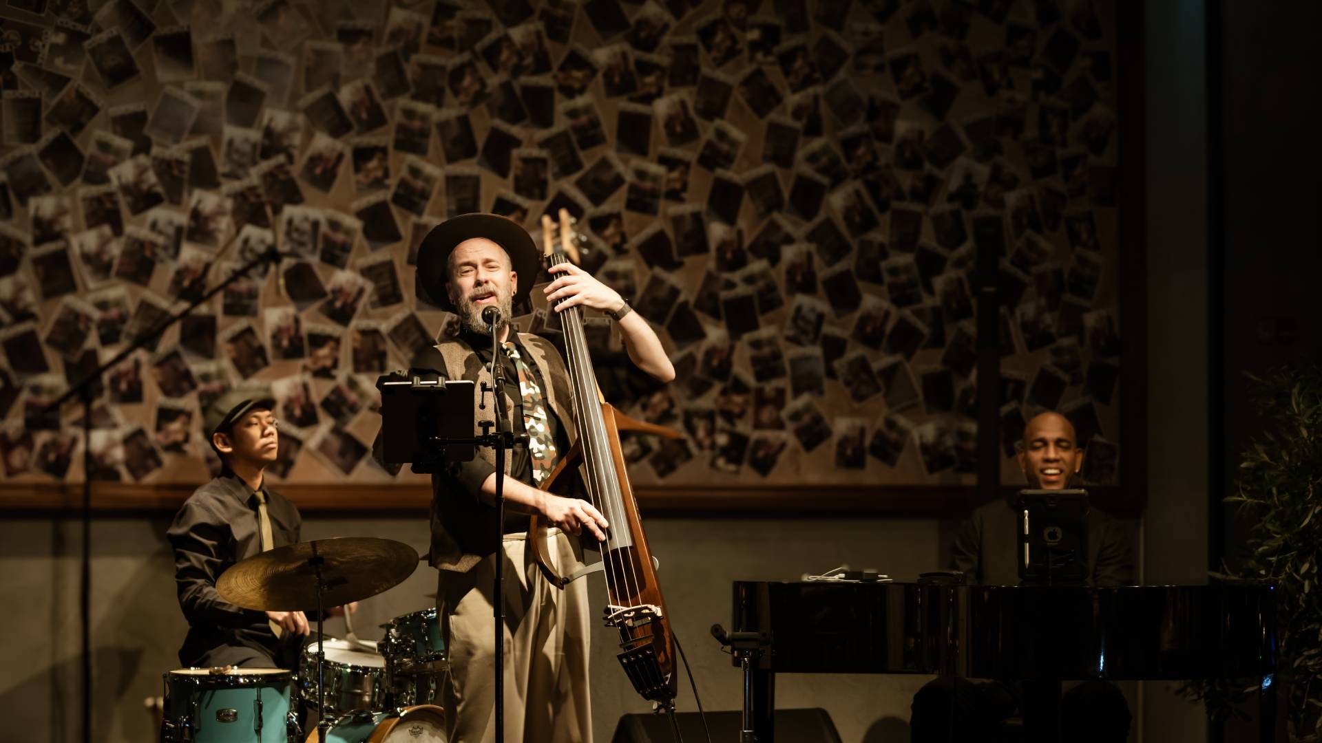 Three-piece jazz trio performing live at Cucina The Palm during Jazz and Juice Nights, featuring upright bass, piano, and drums against decorative wall backdrop.