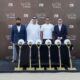 Four executives at MAAIA La Clé groundbreaking event with ceremonial shovels and hard hats at Al Furjan construction site.