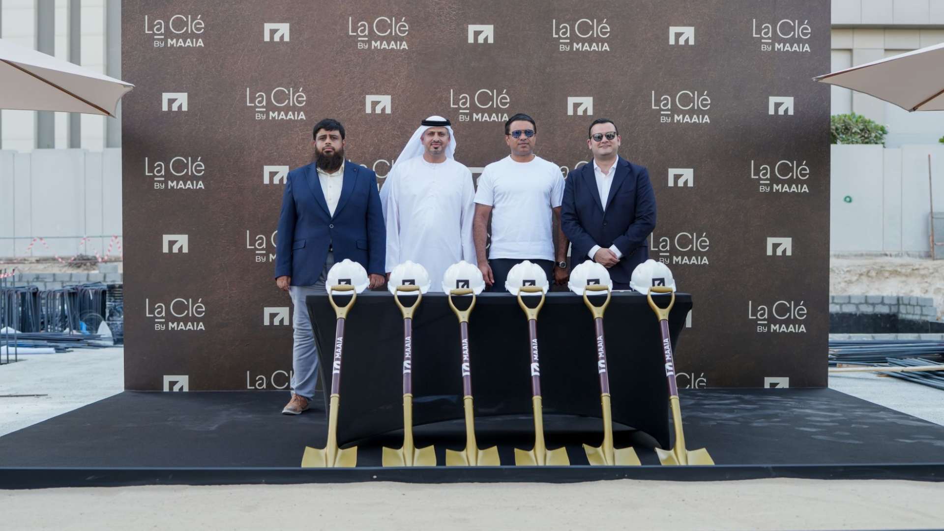 Four executives at MAAIA La Clé groundbreaking event with ceremonial shovels and hard hats at Al Furjan construction site.