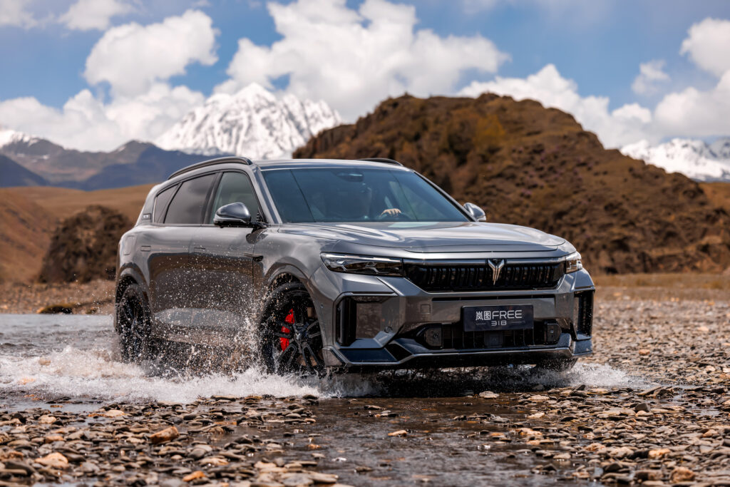 A front-three-quarter shot of a VOYAH FREE driven offroad through shallow waters.