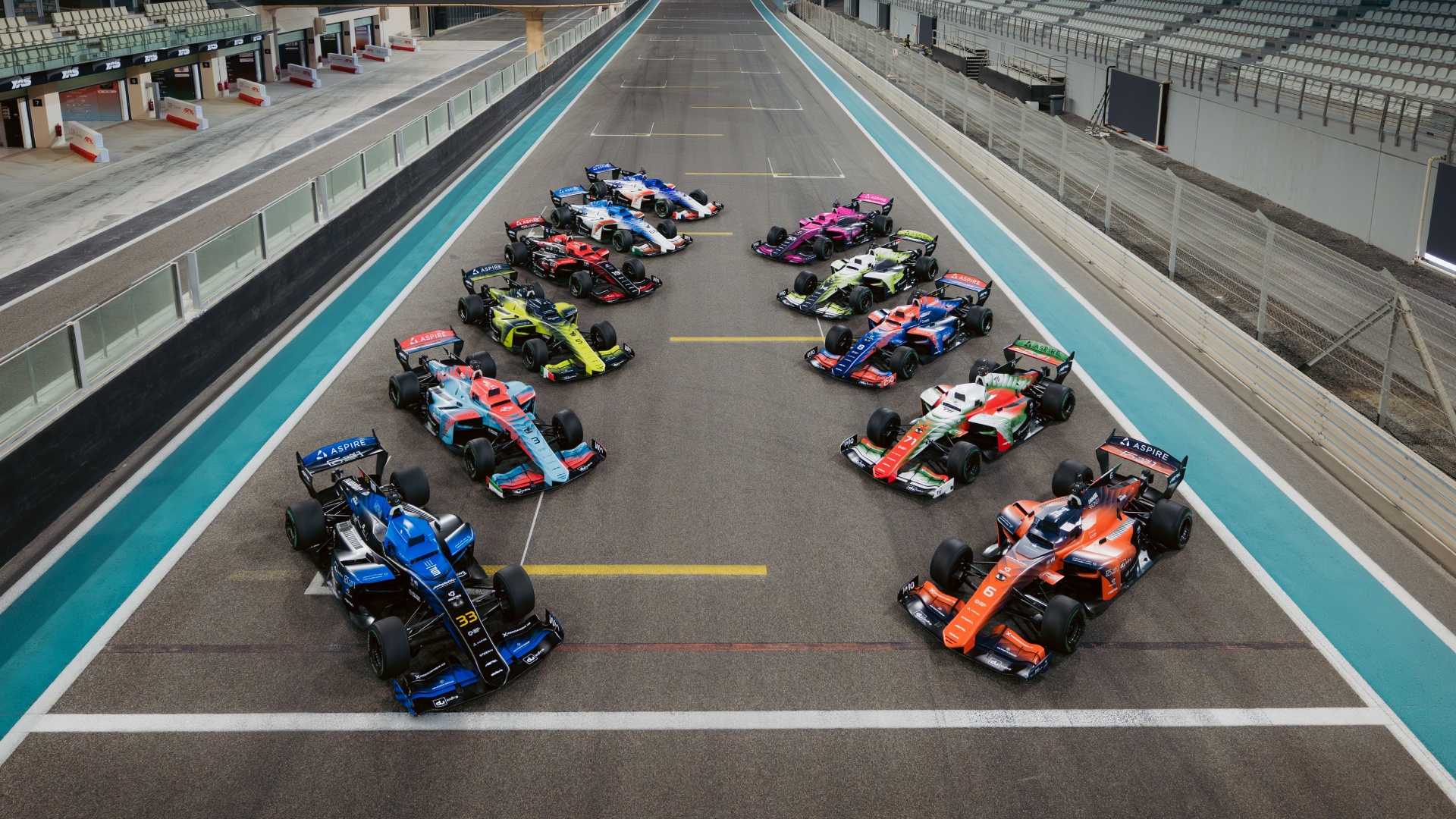 A top-wide-angle shot of all the A2RL race cars parked in formation on the race track.