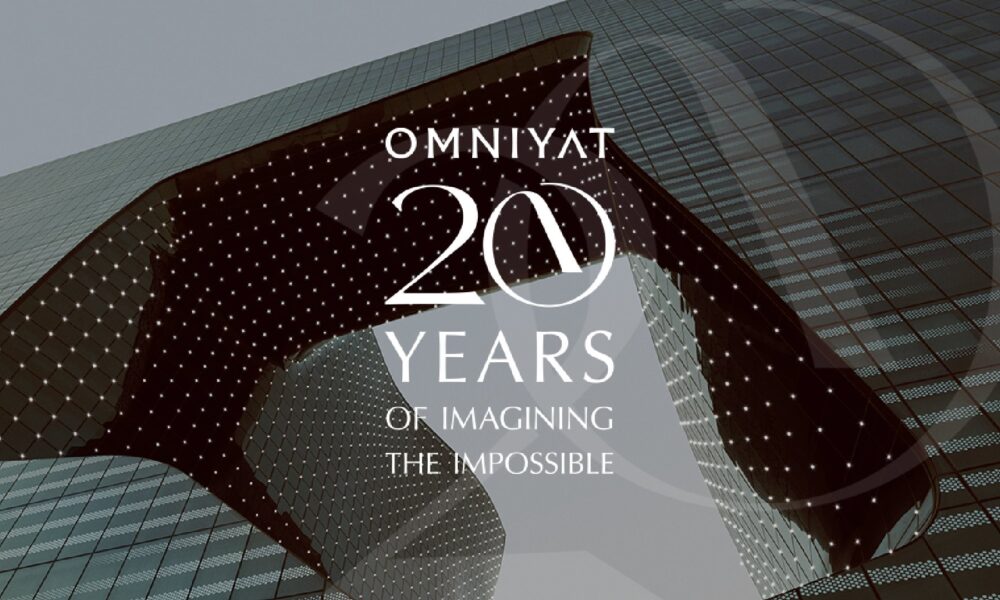 OMNIYAT 20 Years anniversary graphic overlaid on modern architectural building with illuminated facade featuring curved glass and geometric pattern